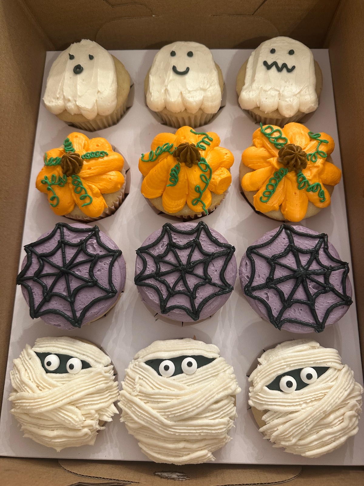 Halloween cupcakes decorated as ghosts, pumpkins, purple spiderwebs, and mummies