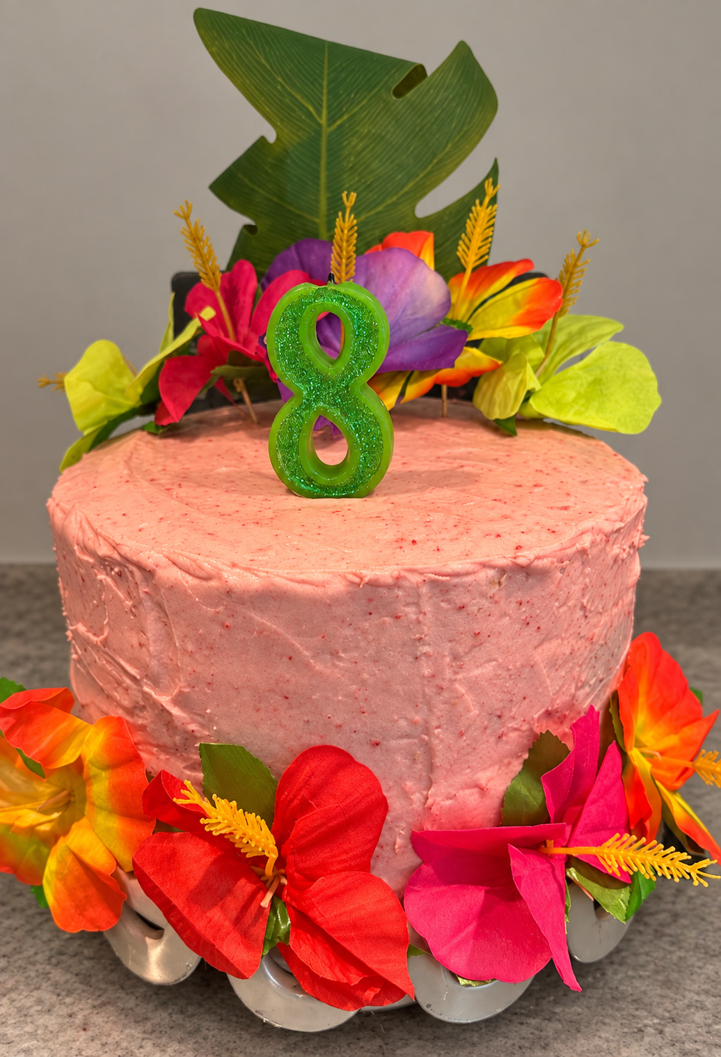 Pink strawberry cake with tropical flowers and a green number eight candle